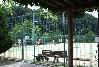 「小野クリーンセンタースポーツ公園テニスコート」の写真。木製屋根下のフェンス外観客ベンチからグラウンドが撮影されている。