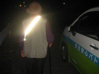 肩にかけた反射テープが光っている、夜道を歩く人の後ろ姿の写真
