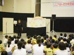 床に座り可愛い絵を飾っている隣で話す女性に注目している園児たちの写真