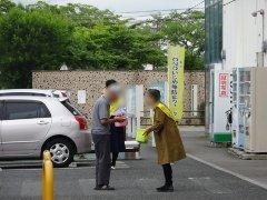 施設駐車場の前でた女性が啓発グッズを男性に渡し話しかけている写真