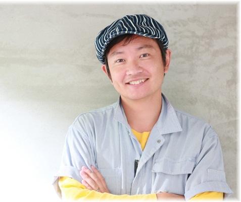 黄色の長袖Tシャツにグレーの半袖シャツを重ね着しハンティング帽をかぶって微笑む山崎清治さんの写真