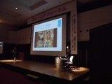 ステージに設置された大型スクリーンの脇で水無田気流さんが講義を行っている写真