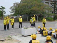 黄色い服を着た青少年補導委員会の話を座りながら聞く児童たちの写真