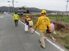 補導員の見守りの中田畑の続く道を下校する児童たちの写真