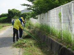 大部小学校。グラウンド横の落ち葉や雑草を除去している職員の写真