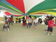 赤、白、緑、黄、青などの色のドーム状の屋根の下で沢山の子供達がデマンドバルーン遊びをしている写真
