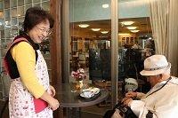 絆カフェの店内でおじいさんのお客さんに接客している女性店員の写真