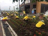 花壇で土を掘っている黄色いユニフォームを着たガーデニングボランティアたちの写真