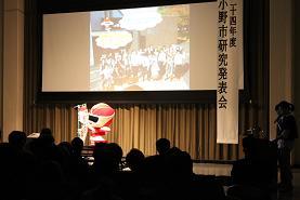 小野市研究発表会で写真が映し出されているスクリーンの前に着ぐるみを着た人が立っている写真