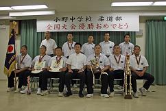 「全国大会優勝おめでとう」と書かれた看板の前での小野中柔道部男子団体の記念写真