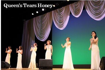 6人の女性で結成されているクイーンズティアーズハニーが、白いドレスを着てステージの上で歌っている写真