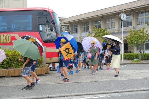 暑さ対策としてのスクールバスを利用して、生徒たちが日傘をさしながら登下校している様子の写真
