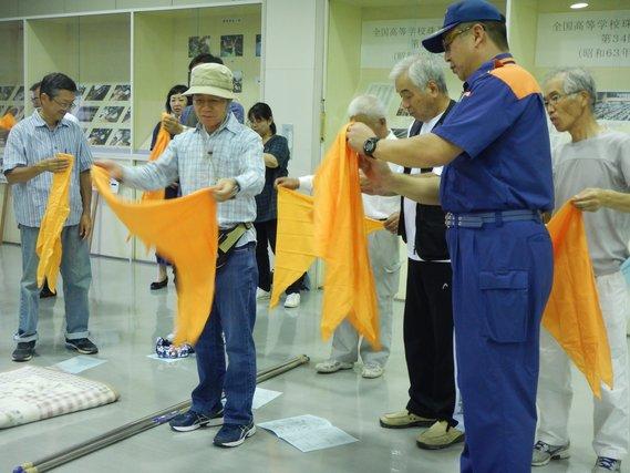 オレンジ色のタオルを手に防災訓練を行っている人たちの写真