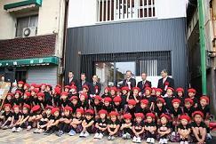 陣屋の町らしさをイメージした白壁と縦格子のデザインの建物の前に、黒い服と赤い三角巾をかぶった子供たちが並んでいる集合写真
