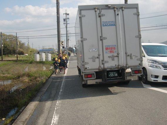 通行車両がすれ違う中、片山高田線の路肩を歩く通学児童の写真