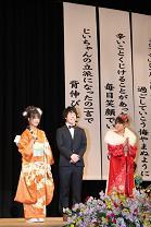 ステージに立っている振袖を着た女性2人とスーツを着た男性1人の写真