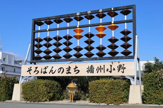 「そろばんのまち 播州小野」と書かれた木の看板の上に建つ、巨大そろばんのモニュメントの写真