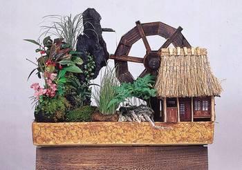 岩や苔、植物や水車、小さな小屋などで箱庭がジオラマで表現されたセンサリーガーデン「あこがれの田舎ぐらし」の写真