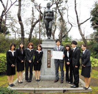 撮影のために成年式発祥の地記念像の前で笑顔で並ぶスーツ姿の青年たちの写真