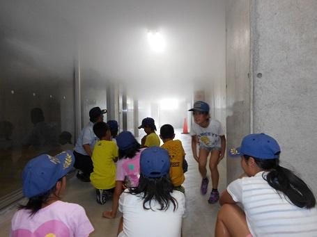 煙が天井付近に充満している通路を体を低くして避難訓練をしている生徒たちの写真