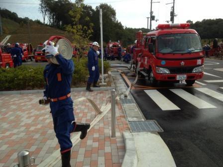 消防車に収納されたホースを肩に担いで運んでいる消防団員の写真