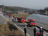 数人の消防隊員が立っている奥で数台の消防車が停車している写真