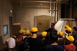 備蓄倉庫の中の備蓄品を説明している消防団職員と説明を受ける生徒たちの写真