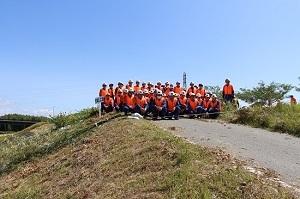 オレンジ色のベストを着た大勢の作業員が土手の上に並んで立っている写真
