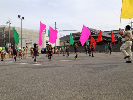 駐車場広場でボーイスカウトの子供らが旗を持ってマーチングをしている写真