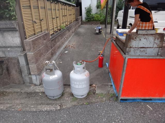 露店の横にガスボンベが2本あって直ぐ近くに消火器があって奥に発電機が置いてある写真