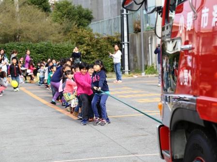 消防車に縄をくくって綱引きをしている子供たちの写真