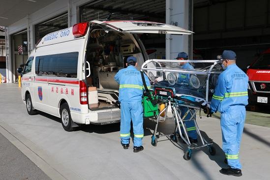 透明な密閉式カプセルにごとストレッチャーに乗せられて救急車まで運ばれている傷病者の写真