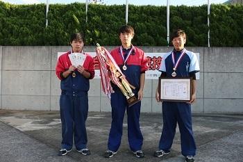 メダルを胸に掛けトロフィーを持つ真ん中の人と、賞状を掲げている右側の人の写真