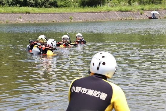 水難救助用の服を着た隊員たちがロープを使い川からの救出訓練を行っている写真