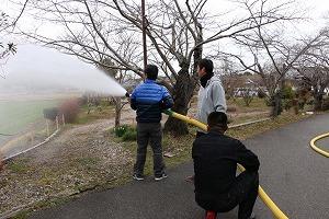 青色や白色のジャケットを着た男性たちが放水作業を行っている写真