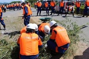 オレンジ色のベストを着た作業員たちが竹を使って作業をしている写真