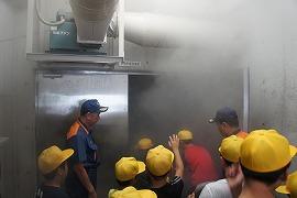 煙が充満している部屋で煙避難を体験している生徒たちと誘導をする消防団職員の写真