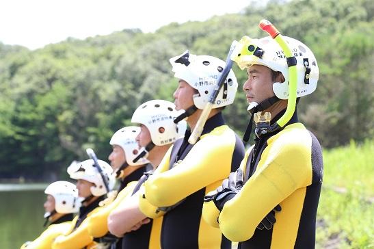 黄色と黒のレスキュースーツを着て白いヘルメットとシュノーケルを装備した隊員たちが腕を組んで並んでいる写真