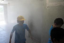 煙が充満している部屋で煙避難を体験している青シャツ生徒2人の写真