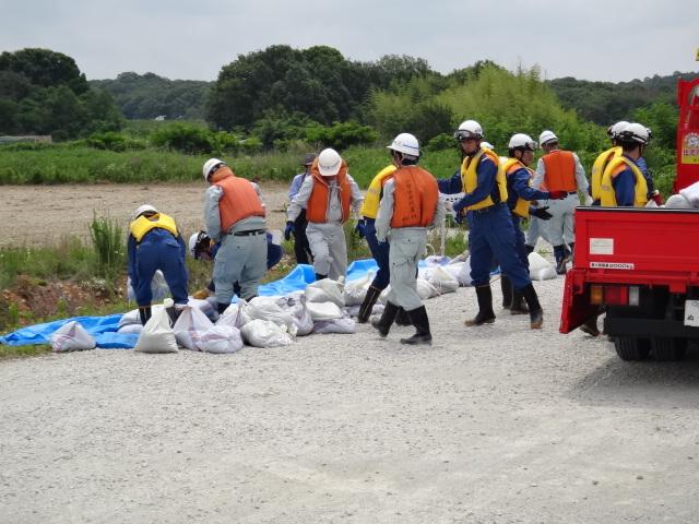オレンジ色や黄色のベストを着た作業員たちが土嚢を運んでいる写真