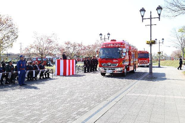 紅白の幕が張られたところの前に消防車が停まっていて、制服を着た消防関係者たちが並んで出迎えている写真
