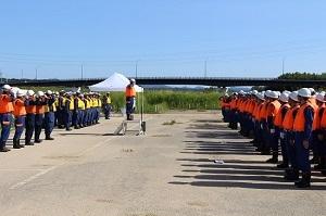 オレンジ色や黄色のベストを着た作業員たちが並んで向き合ってその間に作業員の男性が一人立っている写真