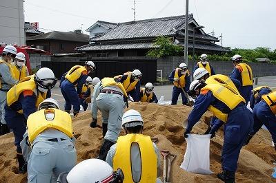 黄色いベストを着て土のうを埋めている作業員たちの写真