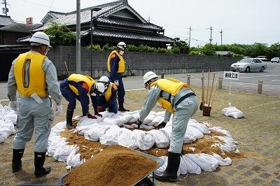 黄色いベストを着た4人の作業員たちが円形になって土のうを積んでいる写真