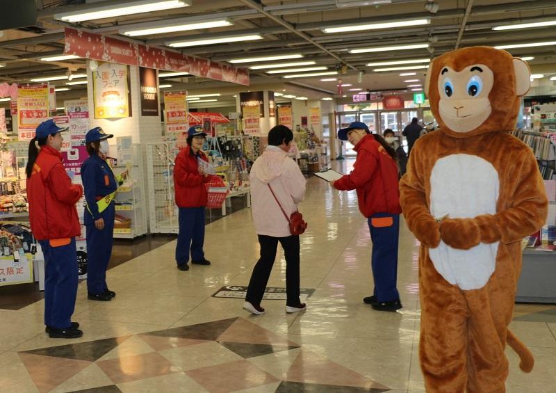 広い店内で猿のマスコットと女性消防職員たちがチラシを配りながら火災予防を呼びかけている写真