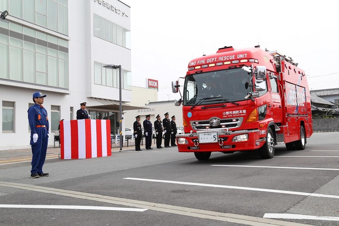 制服を着た消防関係者たちが立っている前に消防車が停まっている写真