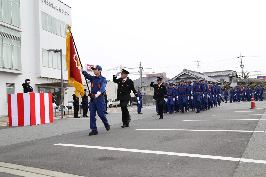 制服を着た消防関係者たちが敬礼しながら行進している写真