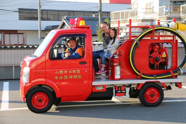 小型の消防車に乗車している隊員と荷台の助手席に乗っている親子の写真