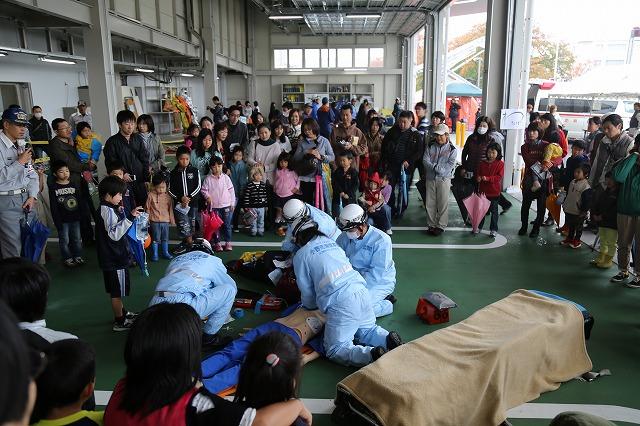 実際の救助活動を彷彿とさせる人形を使ったデモを行う4人の隊員たちとそれを見守る家族連れの参加者たちの写真