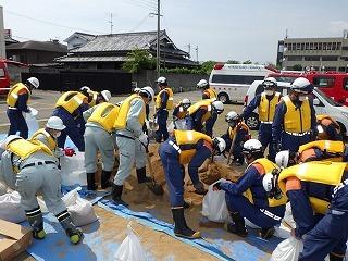 ヘルメットを被った消防隊員と作業員が土のうの作製している写真